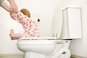 Baby girl (12-15 months) sitting on toilet, holding mother's hands