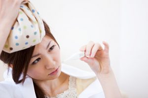 Young woman with ice pack on her head looking at thermometer